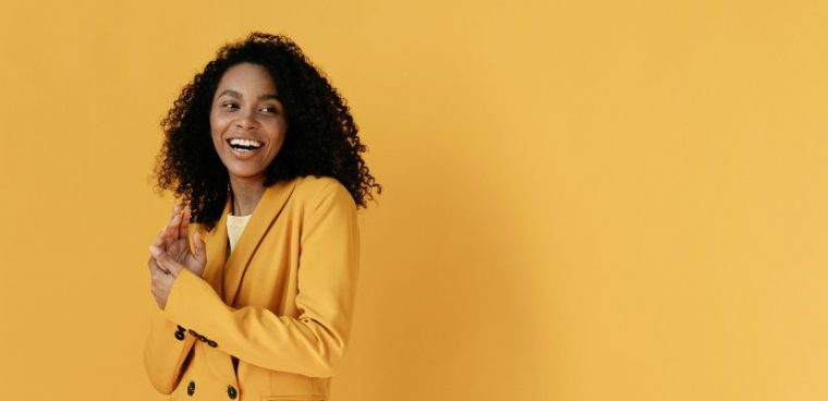 uśmiechnięta kobieta ubrana w żółty garnitur stoi na tle ściany